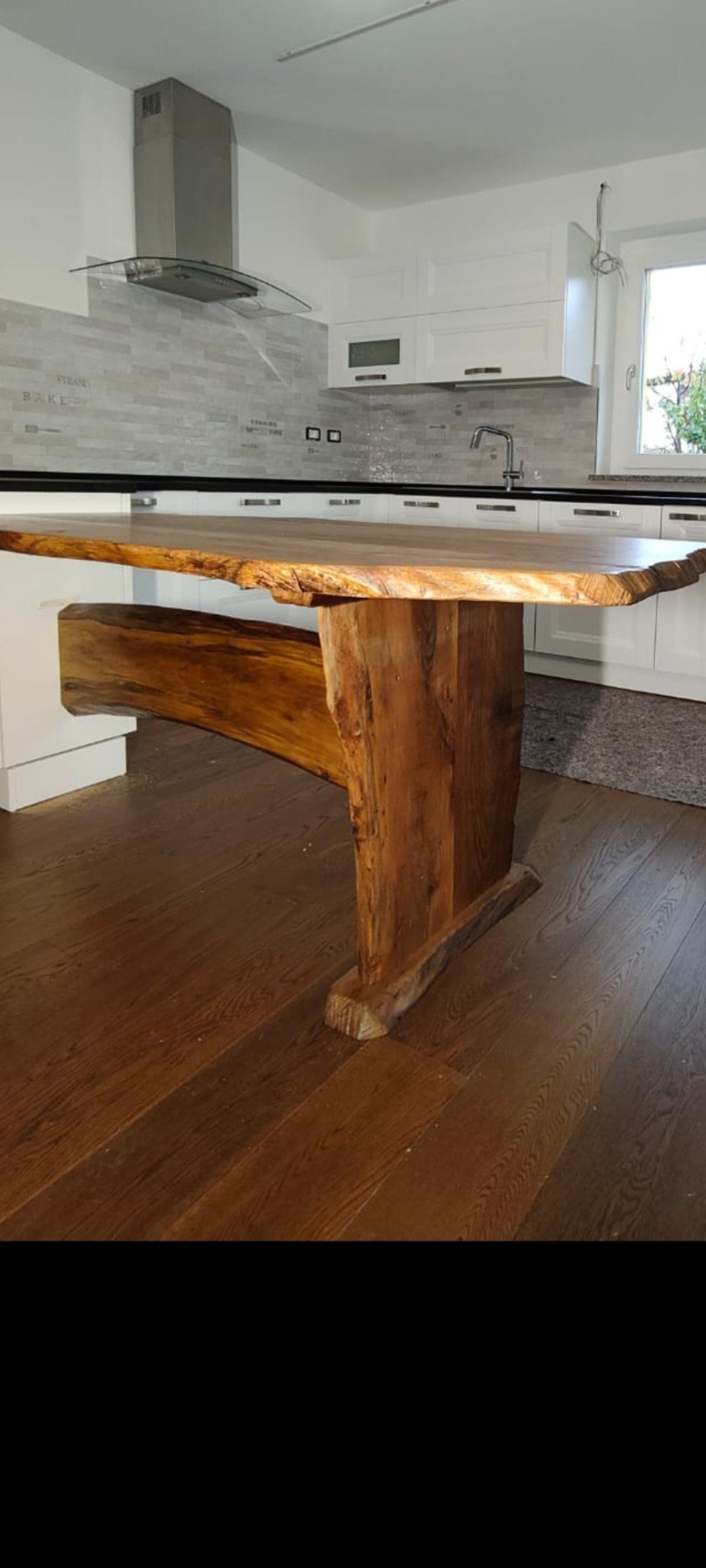 Tavolo da pranzo rustico in legno in una luminosa cucina moderna con mobili bianchi e cappa aspirante.