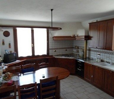 Ampia cucina con mobili in legno, pavimento piastrellato, tavolo rotondo e grande finestra sopra il lavello.