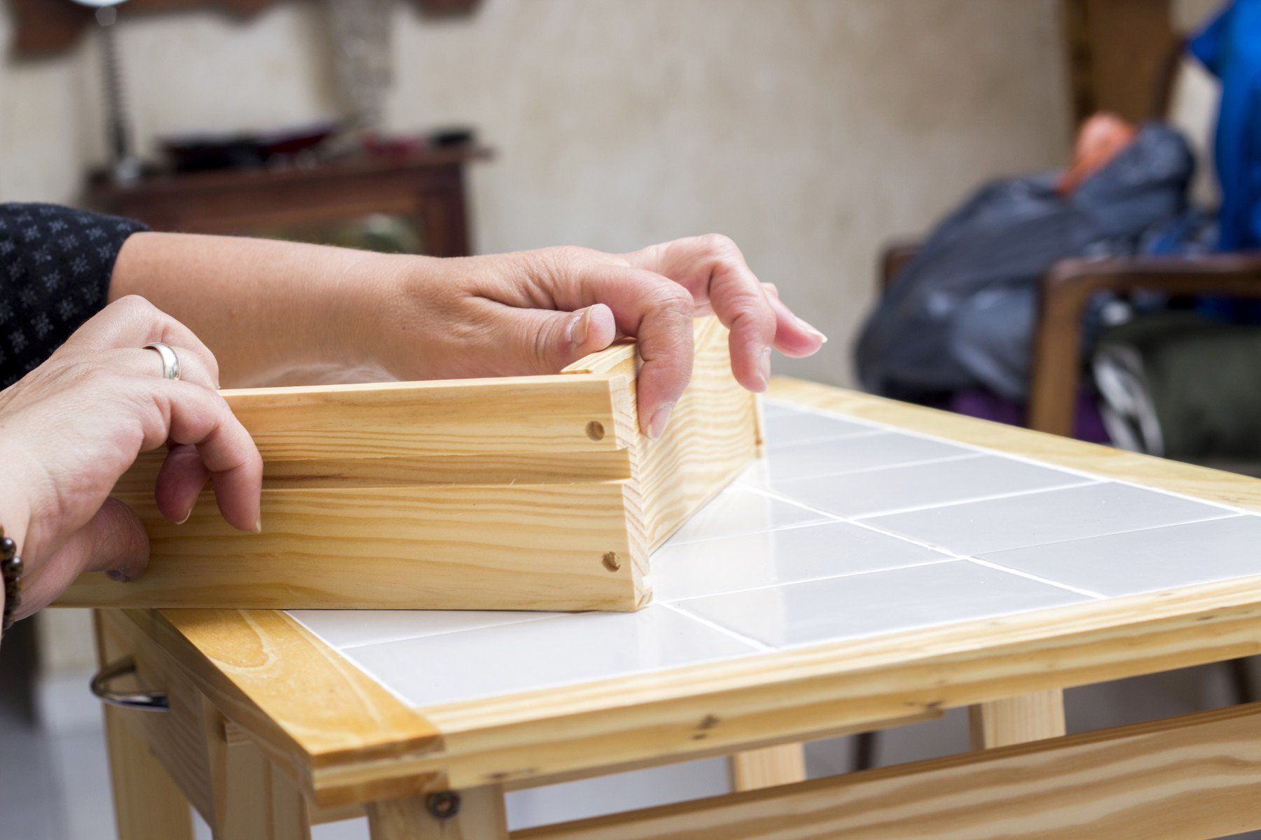 Mani che assemblano una scatola di legno chiaro su un tavolo da lavoro piastrellato