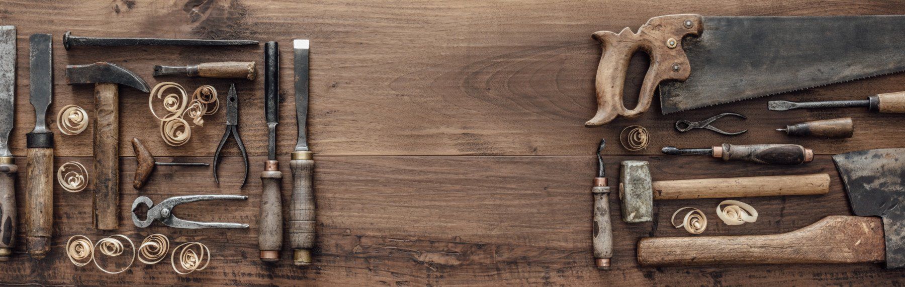 Attrezzi e materiali rustici per la lavorazione del legno, disposti su un tavolo di legno, con seghe, morsetti e utensili manuali.