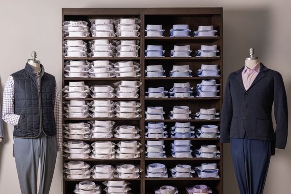 Men's shirts neatly stacked on shelves in a retail setting, flanked by mannequins wearing clothing items.