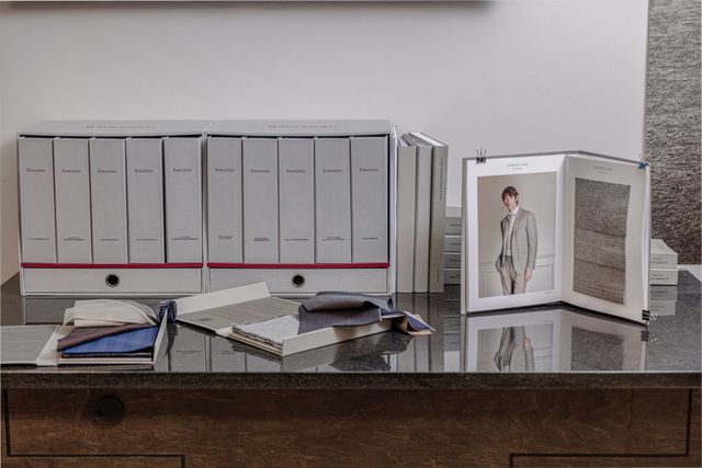 Fabric samples and binders on a desk with a man's photo, likely a design studio or showroom.