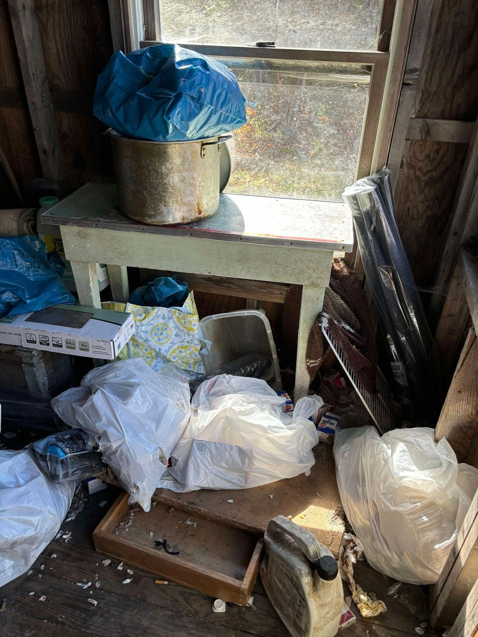Cluttered storage space with bags, boxes, and a small table by a window