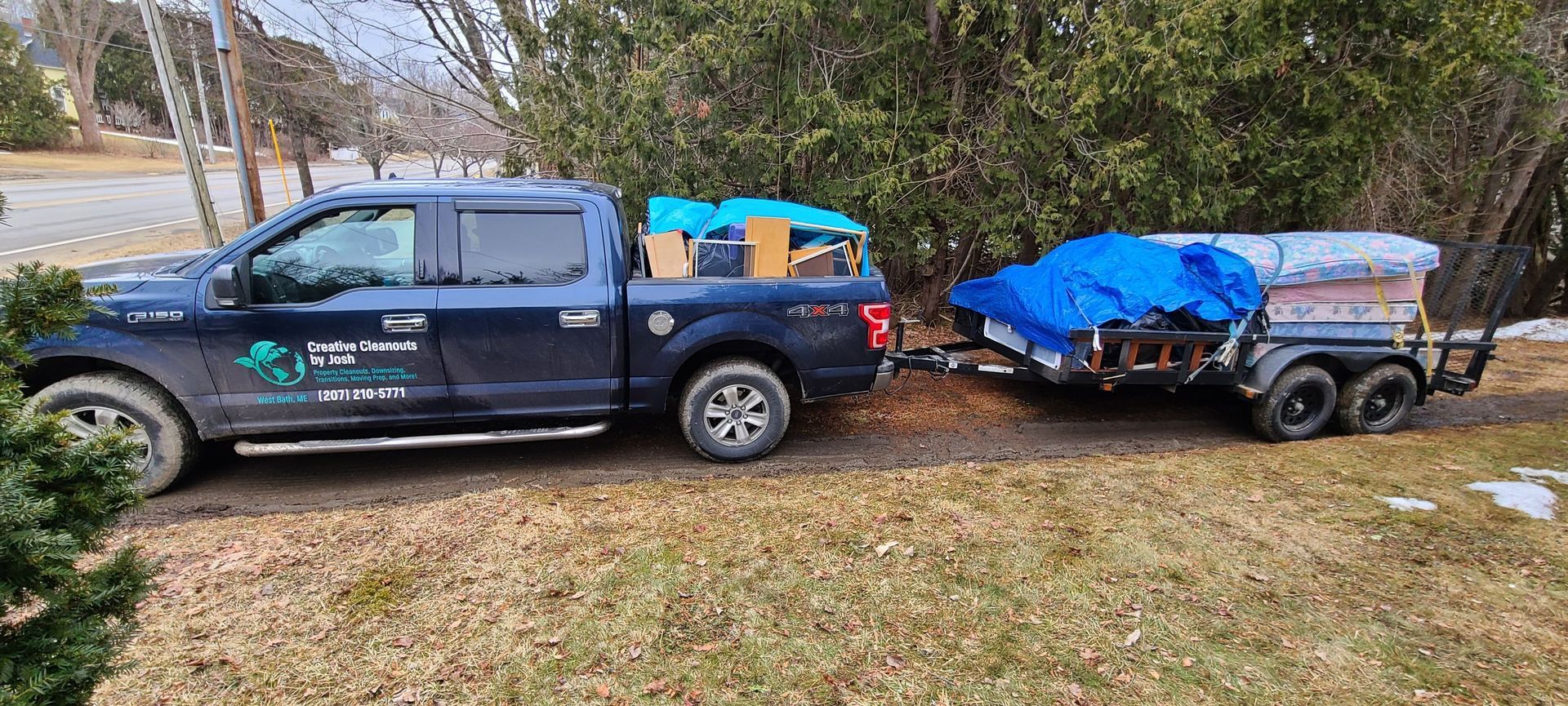 Blue pickup truck towing a small utility trailer loaded with covered cargo on a roadside