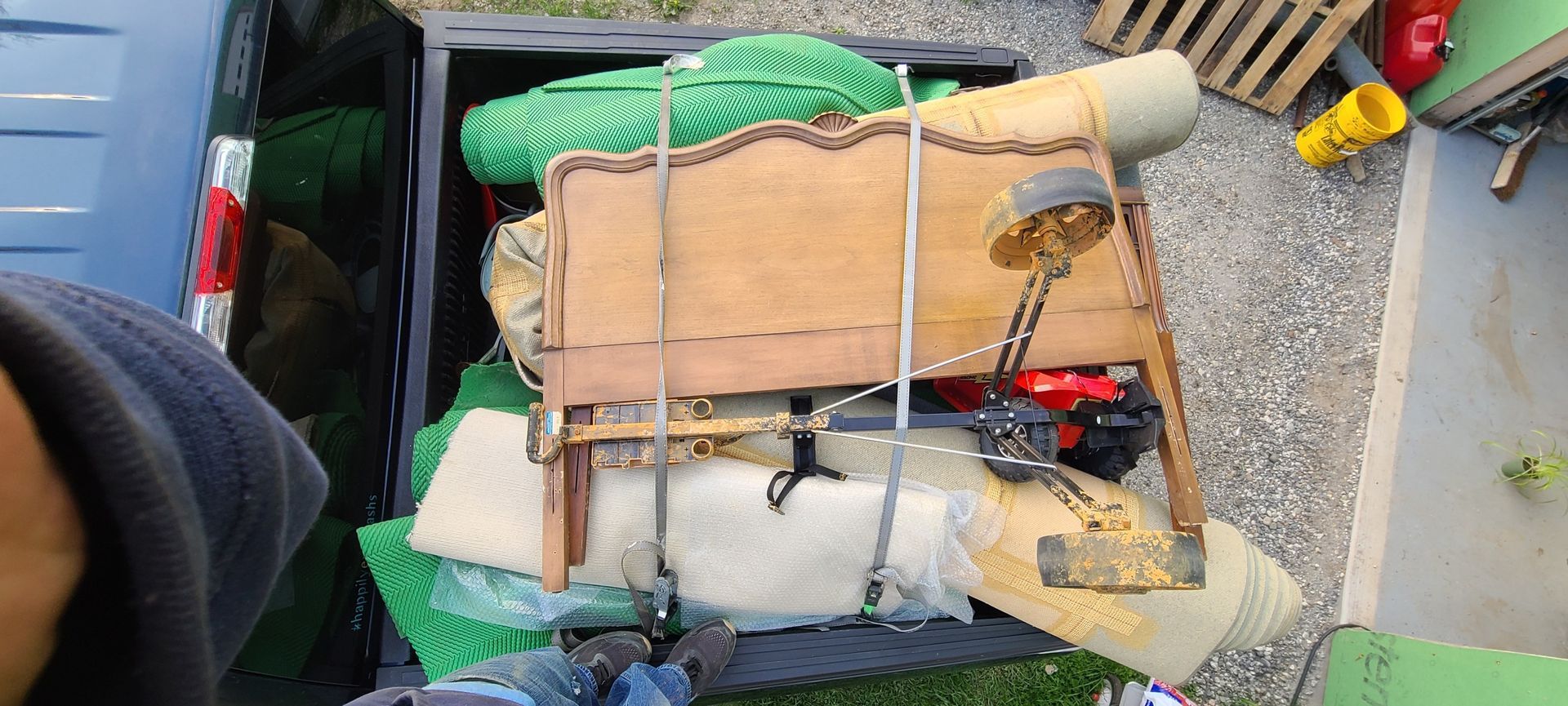 Cart of strapped-down goods with wooden boards, green netting, and tools on a paved surface
