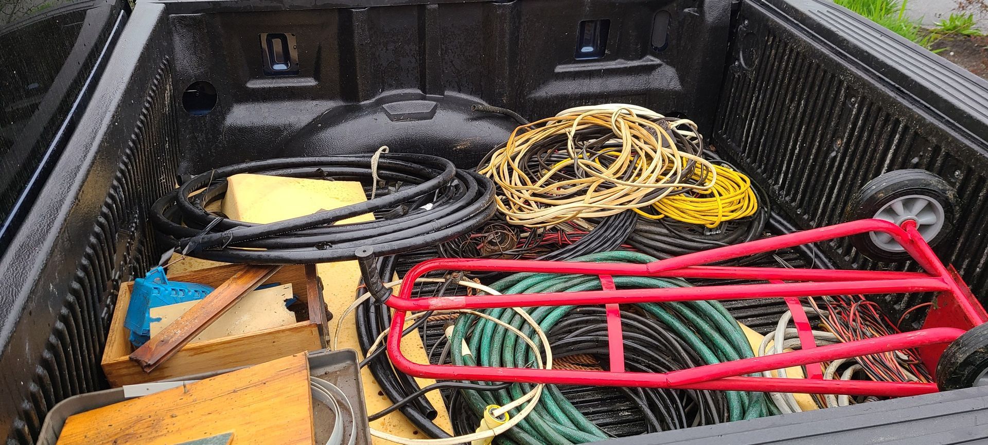 Pickup truck bed filled with coiled cables, tools, and a red metal frame on a black liner