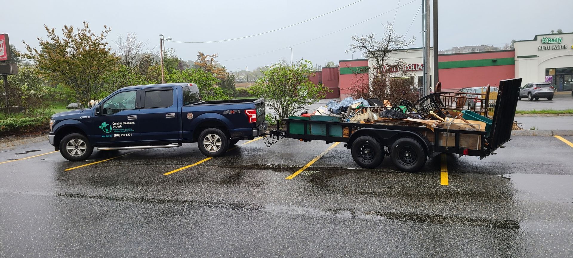 Black pickup truck towing a loaded trailer in a wet parking lot on a rainy day