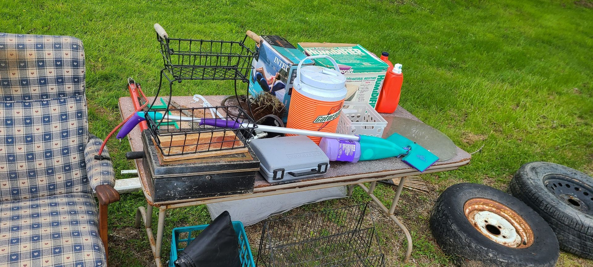 Miscellaneous tools and supplies on a metal cart beside a lawn, with a chair and tire nearby