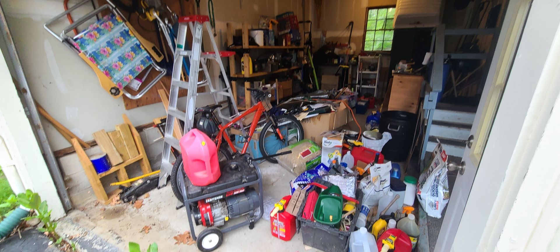 Cluttered garage with tools, ladders, lawn equipment, and various storage items scattered around.