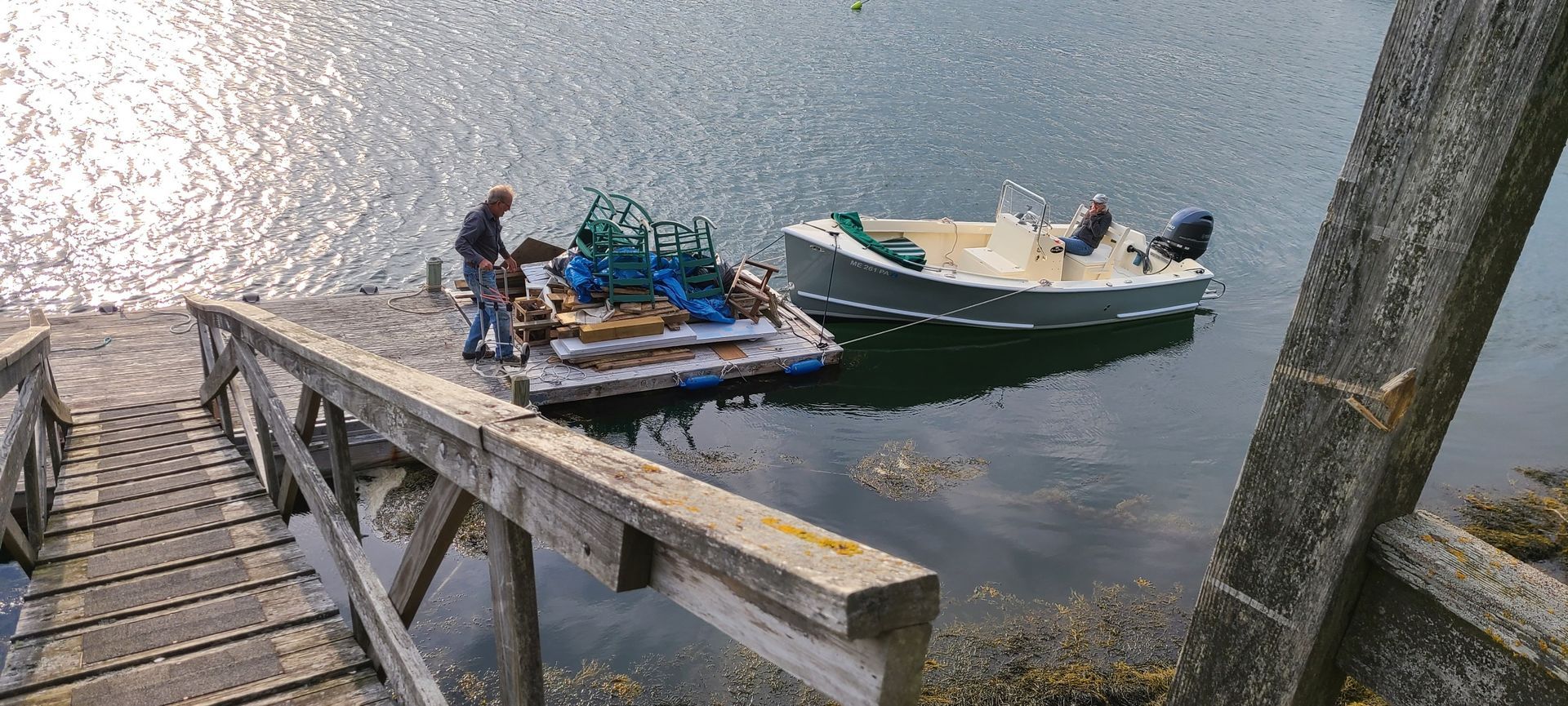 Two small boats moored beside a wooden dock on calm water, with people working on one boat.