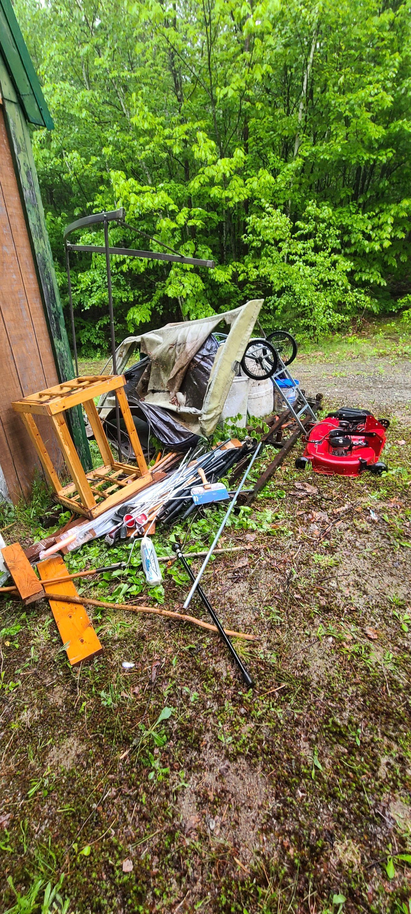 Damaged orange scooter and debris beside a rusted fence in a wooded area