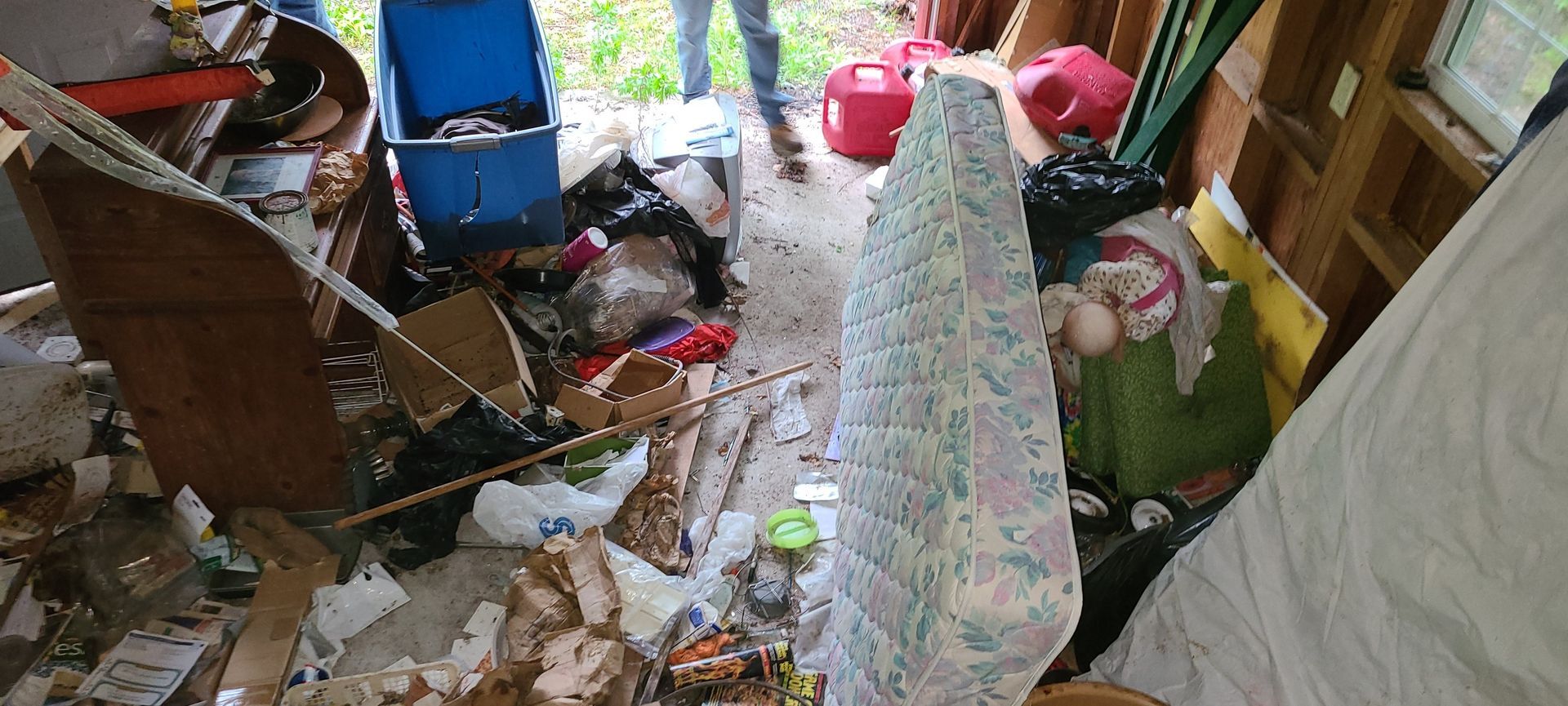 Cluttered room with piles of trash, bottles, and household items around a bed or cot.