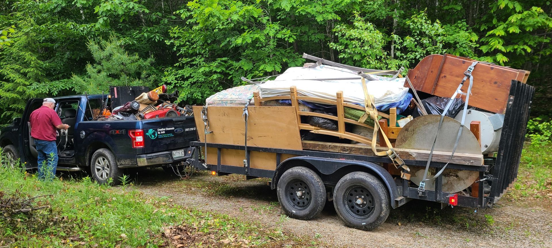 Black pickup towing a loaded utility trailer on a muddy forest road