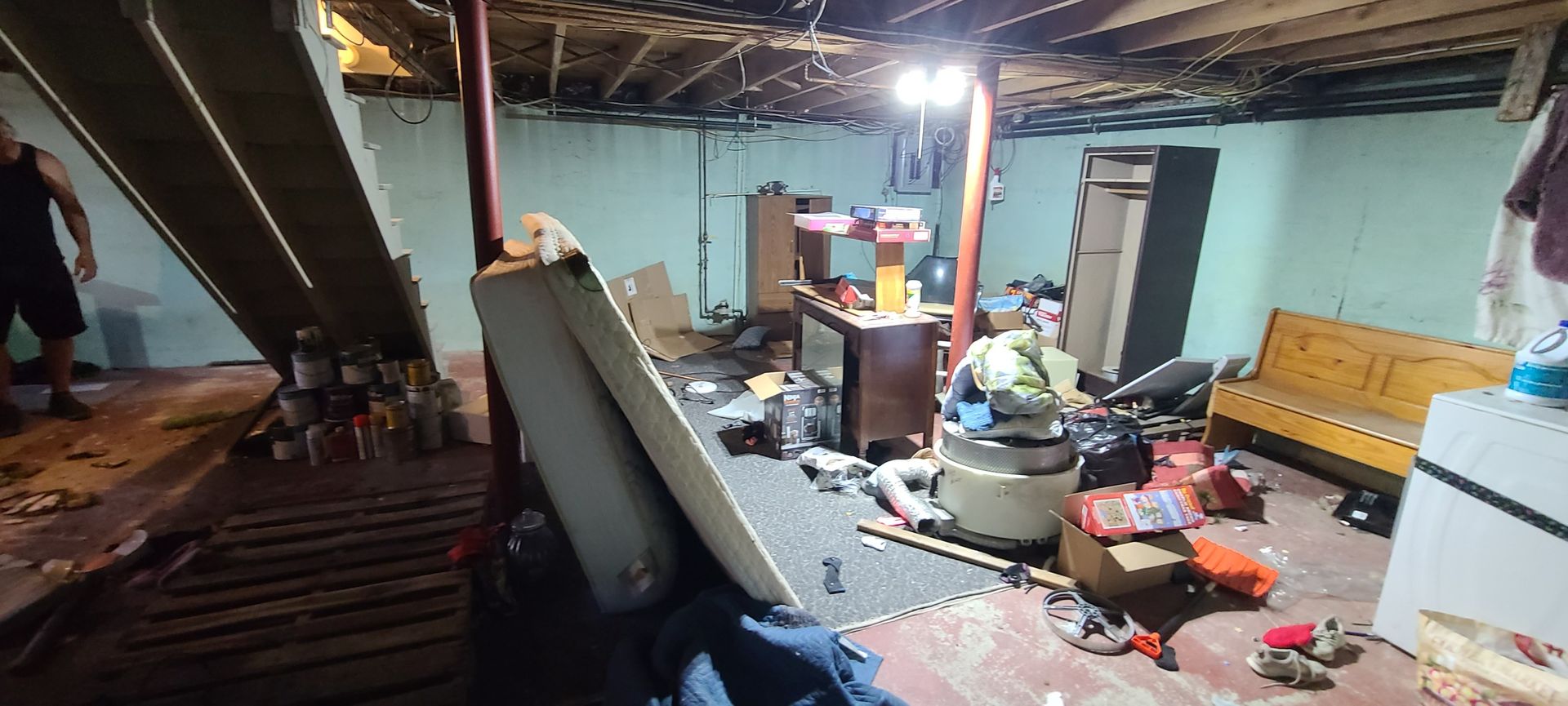 Cluttered room with exposed wooden ceiling, scattered items, and a yellow bench along the wall.