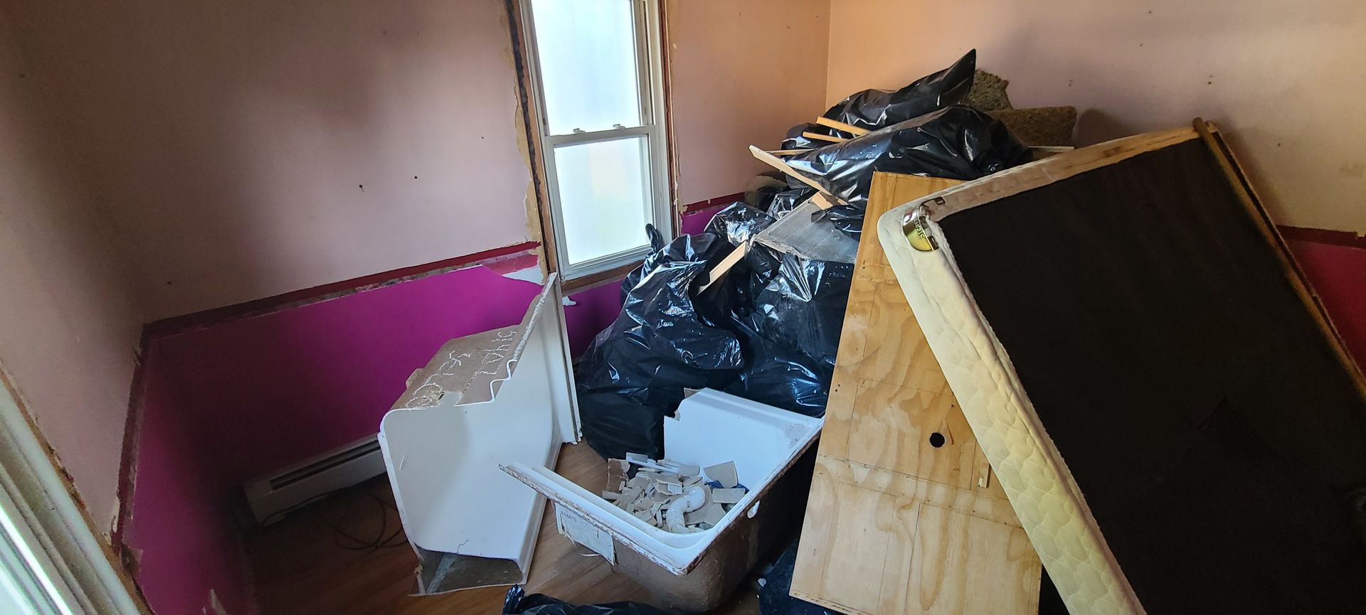 Cluttered room with a pile of trash, boxes, and a large wooden panel leaning against the wall