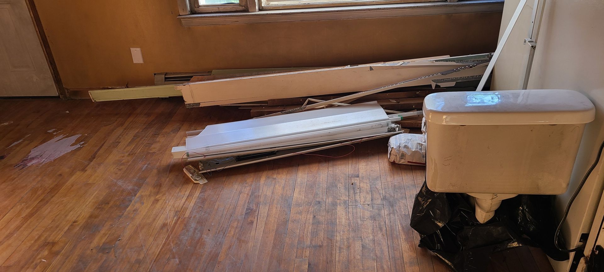 Damaged room with broken floorboards and a white appliance near a window