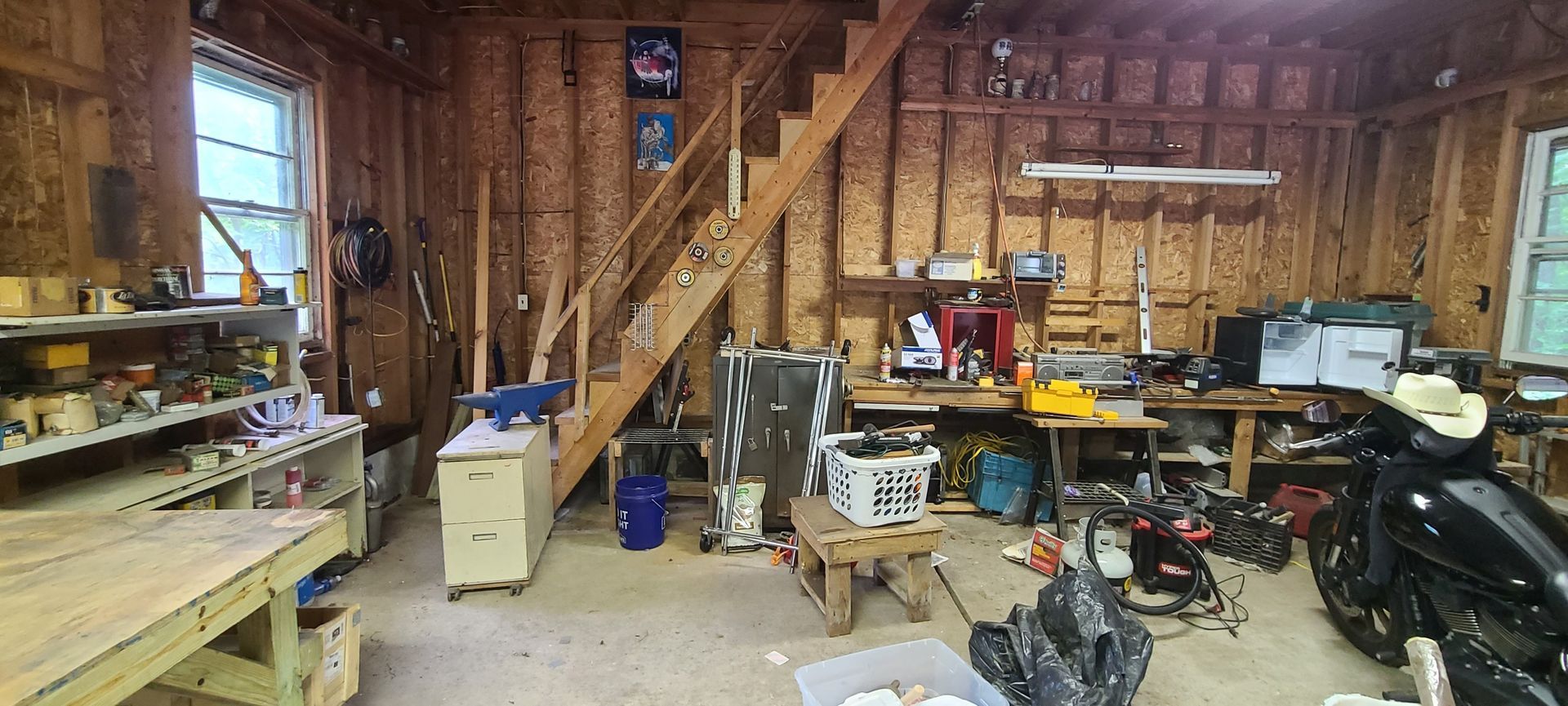 Cluttered workshop with tools, shelves, stairs, and equipment in a wood-paneled garage