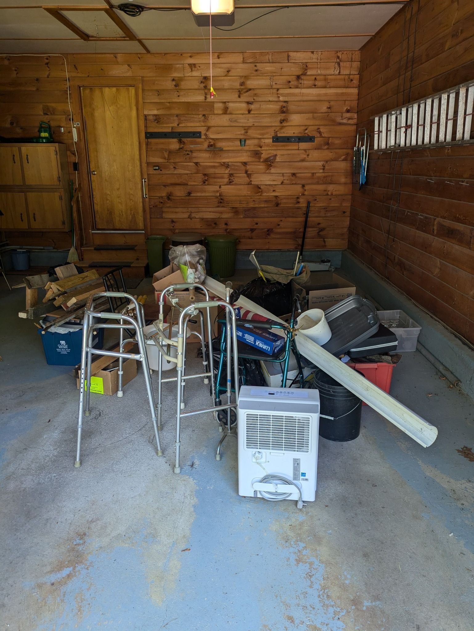 Cluttered garage with scattered tools, bins, and a walker on the concrete floor.