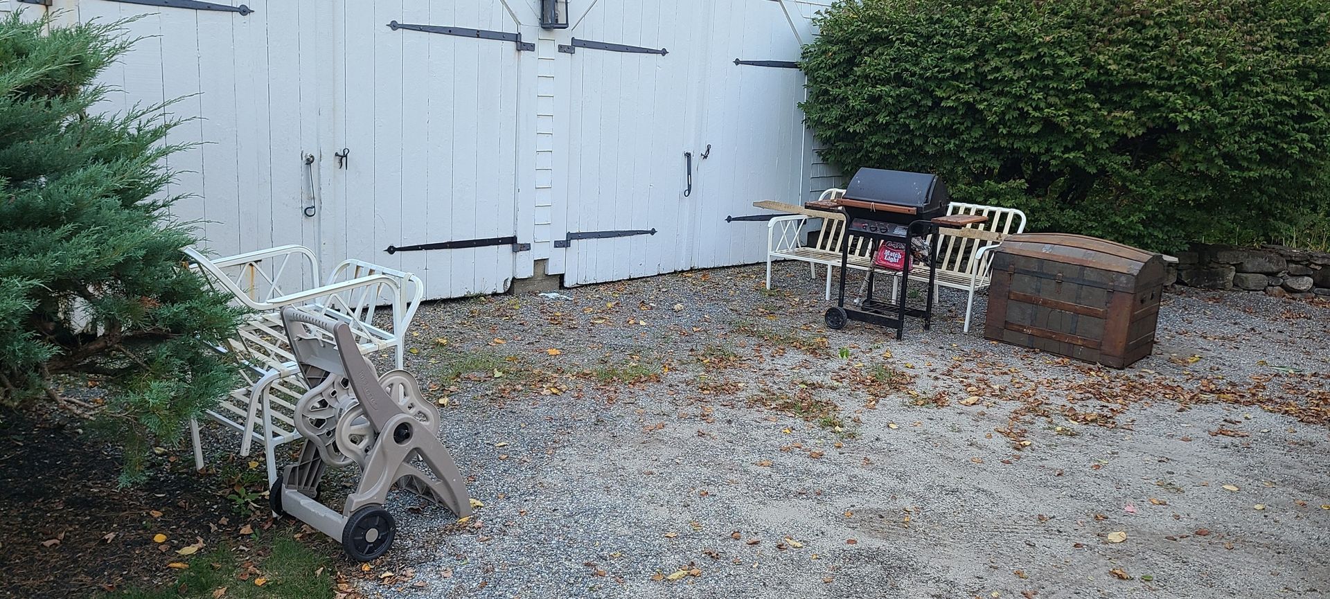 Backyard patio with gravel, white fence, chair, grill, and a small table beside a hedge