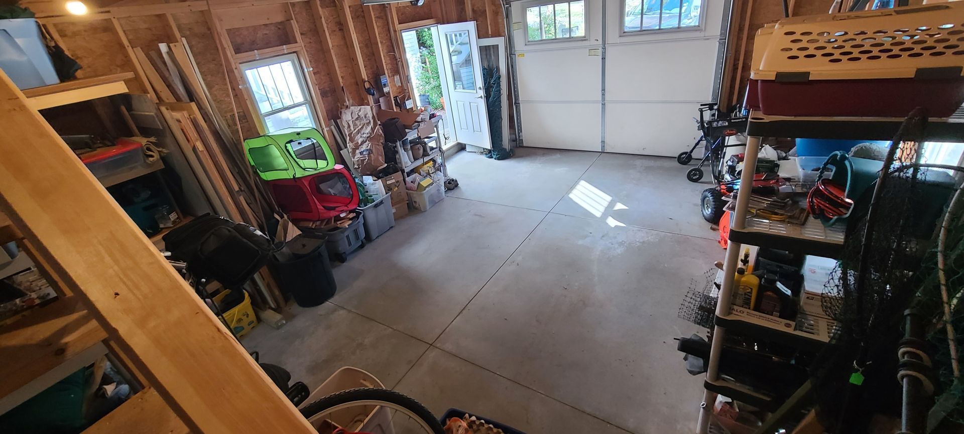 Empty garage interior with concrete floor, shelves, tools, and an open door to daylight