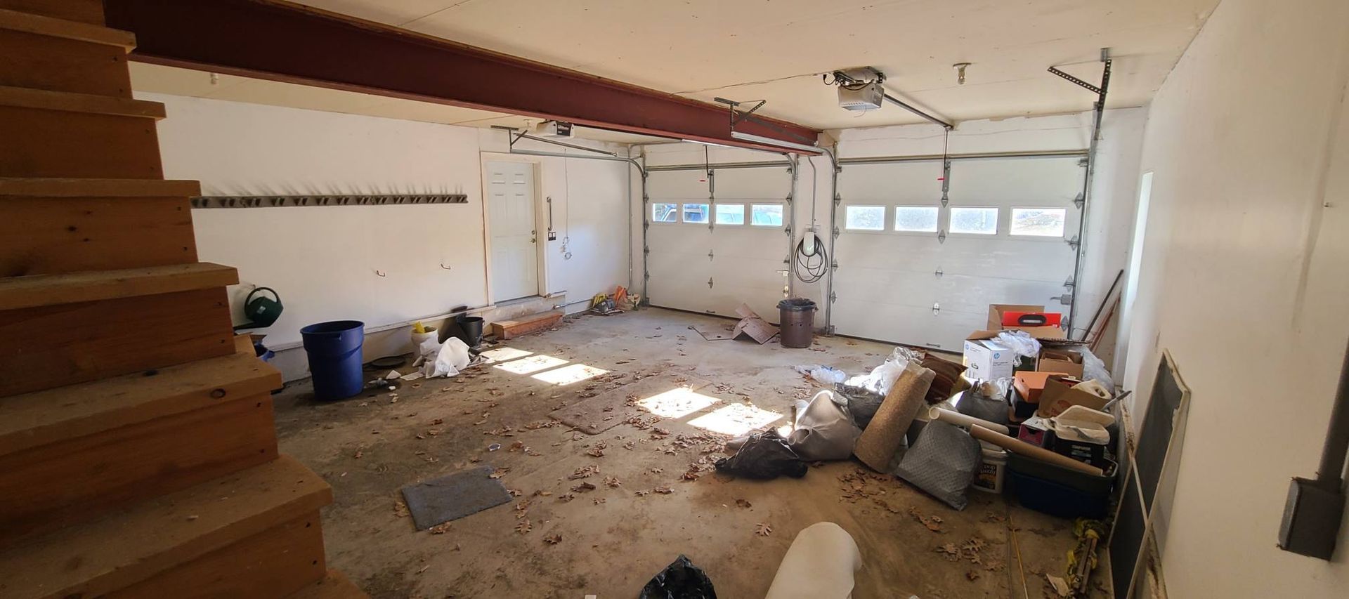 Messy unfinished room with exposed ceiling, scattered tools, and construction debris near windows