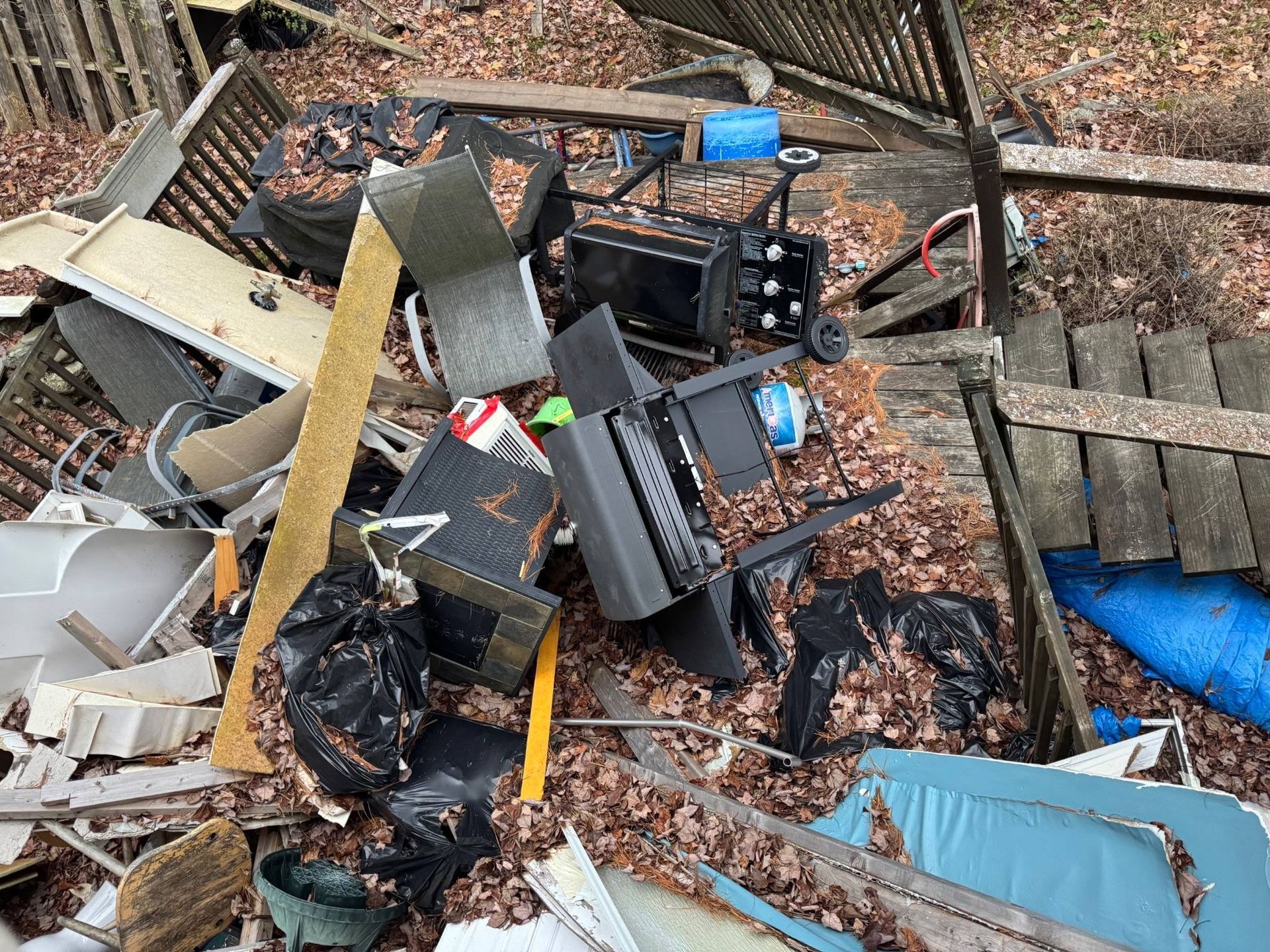 Pile of damaged household debris and furniture in an outdoor yard, with blue tarp and brick steps nearby