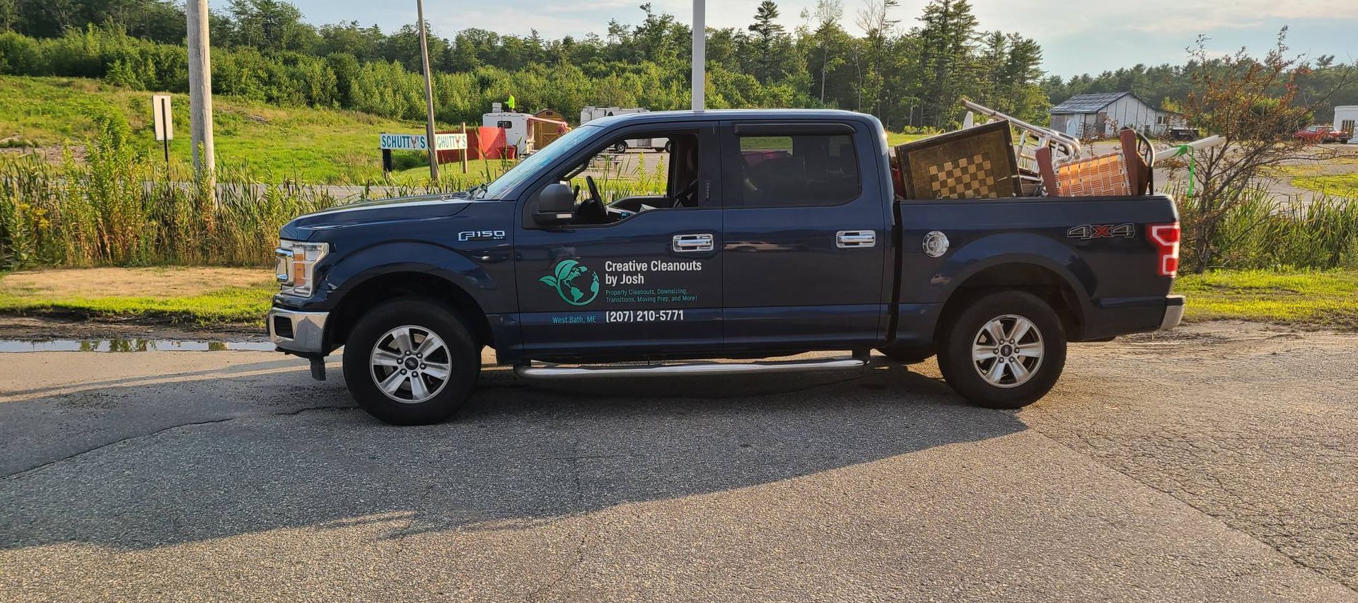 Dark blue pickup truck parked on a gravel road beside green fields and trees