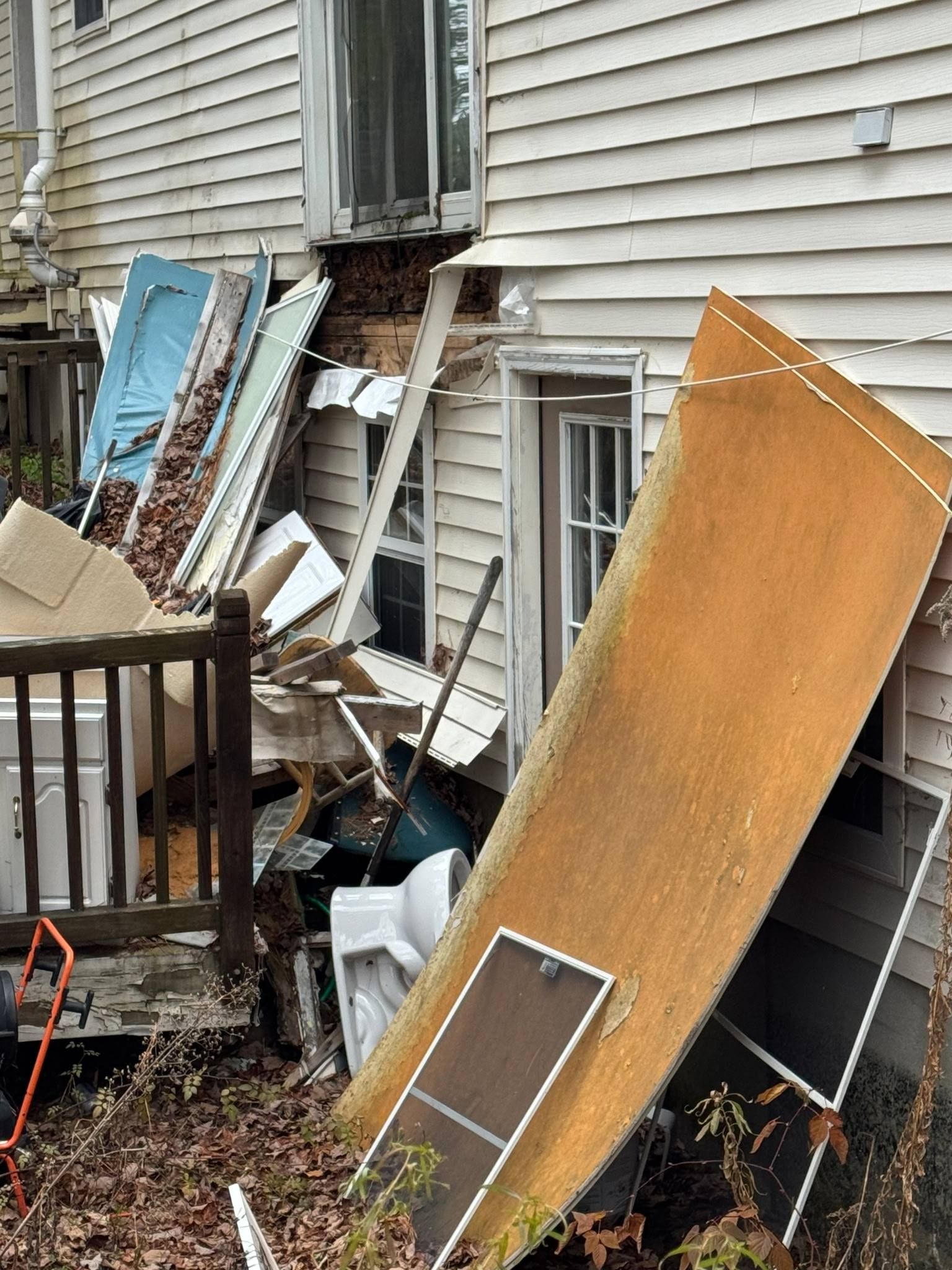 Debris and damaged panels piled against a house exterior after a storm or demolition