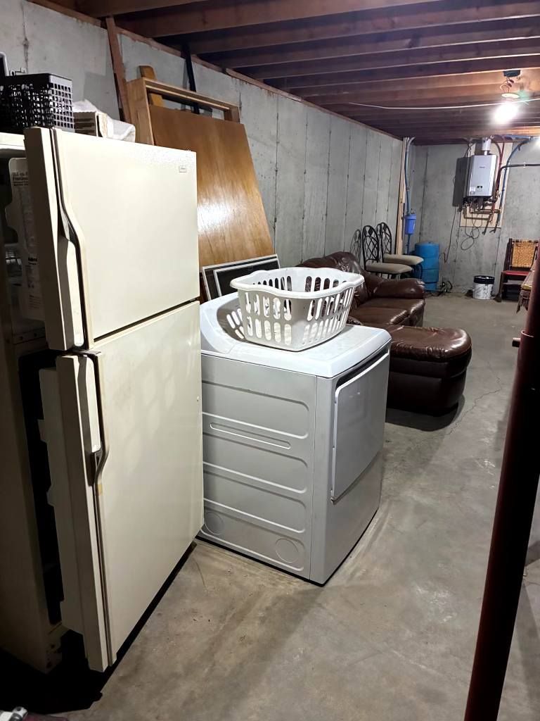 Basement laundry area with a white refrigerator, washing machine, and brown sofa under exposed beams