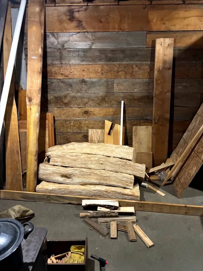 Stacked firewood and rough wooden beams inside a rustic shed or storage area.