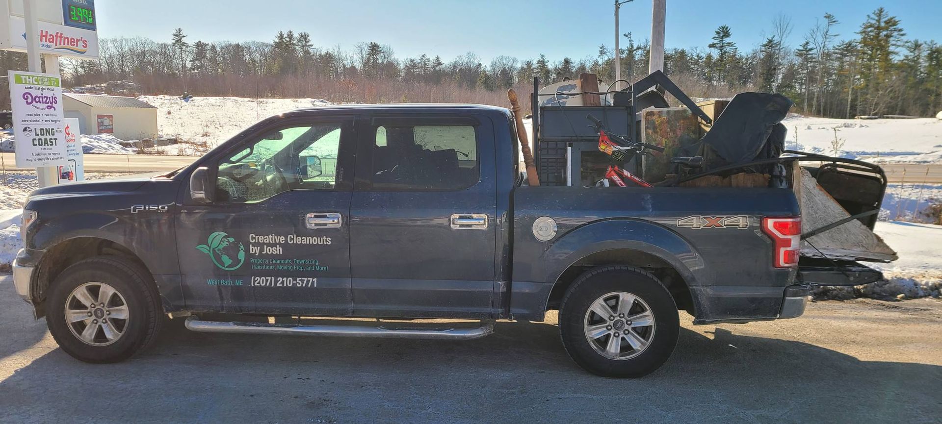 Blue pickup truck with company logo, loaded with equipment in the bed, parked outdoors in a lot.