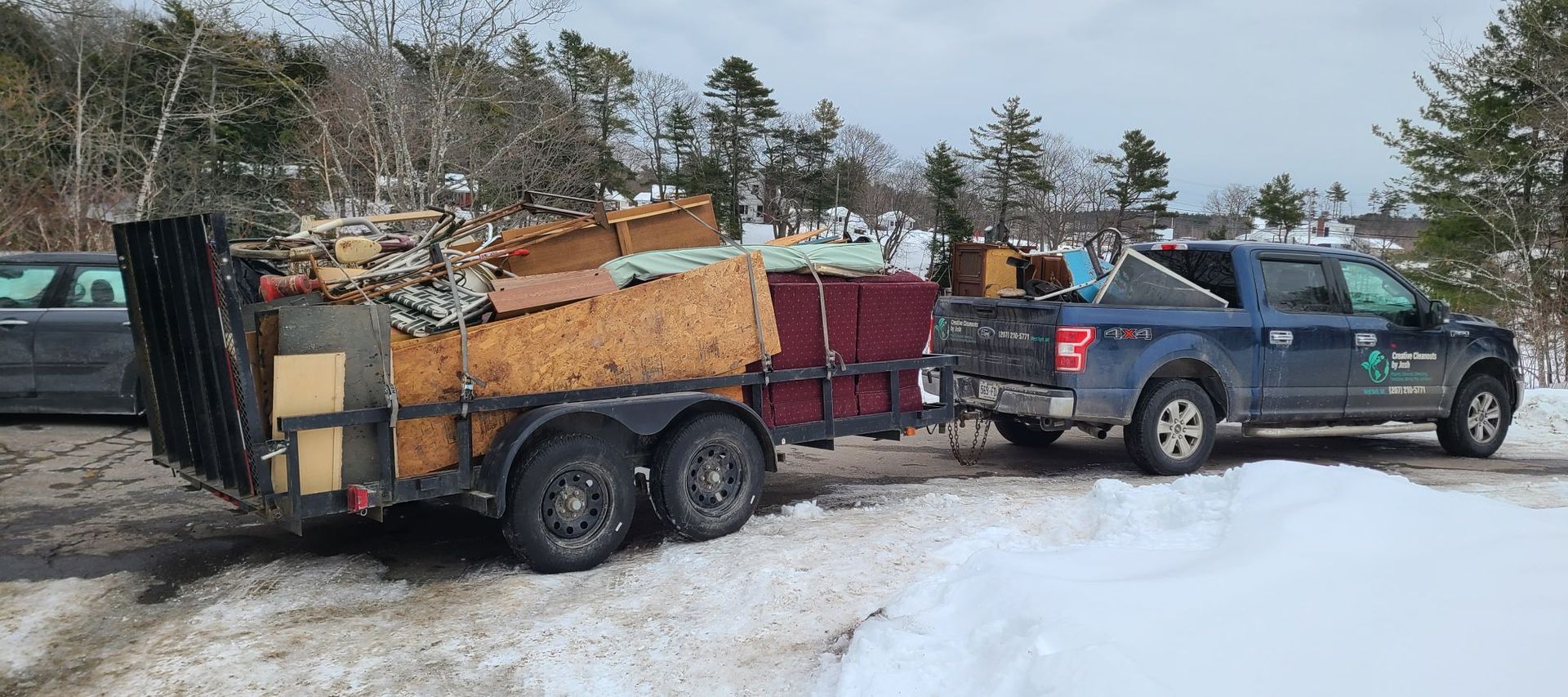 Blue pickup towing a trailer loaded with furniture on a snowy roadside