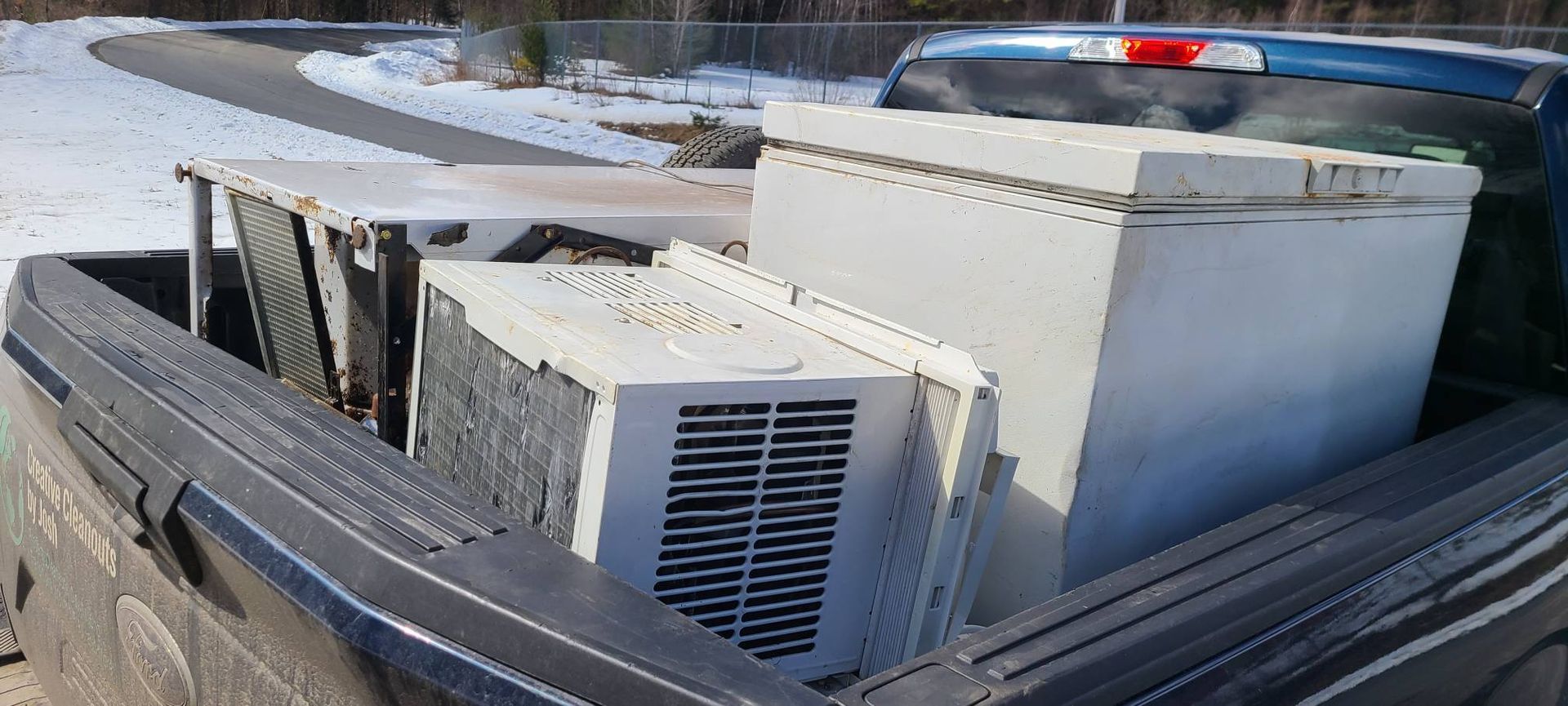 White HVAC unit and metal equipment strapped in pickup truck bed on a snowy road