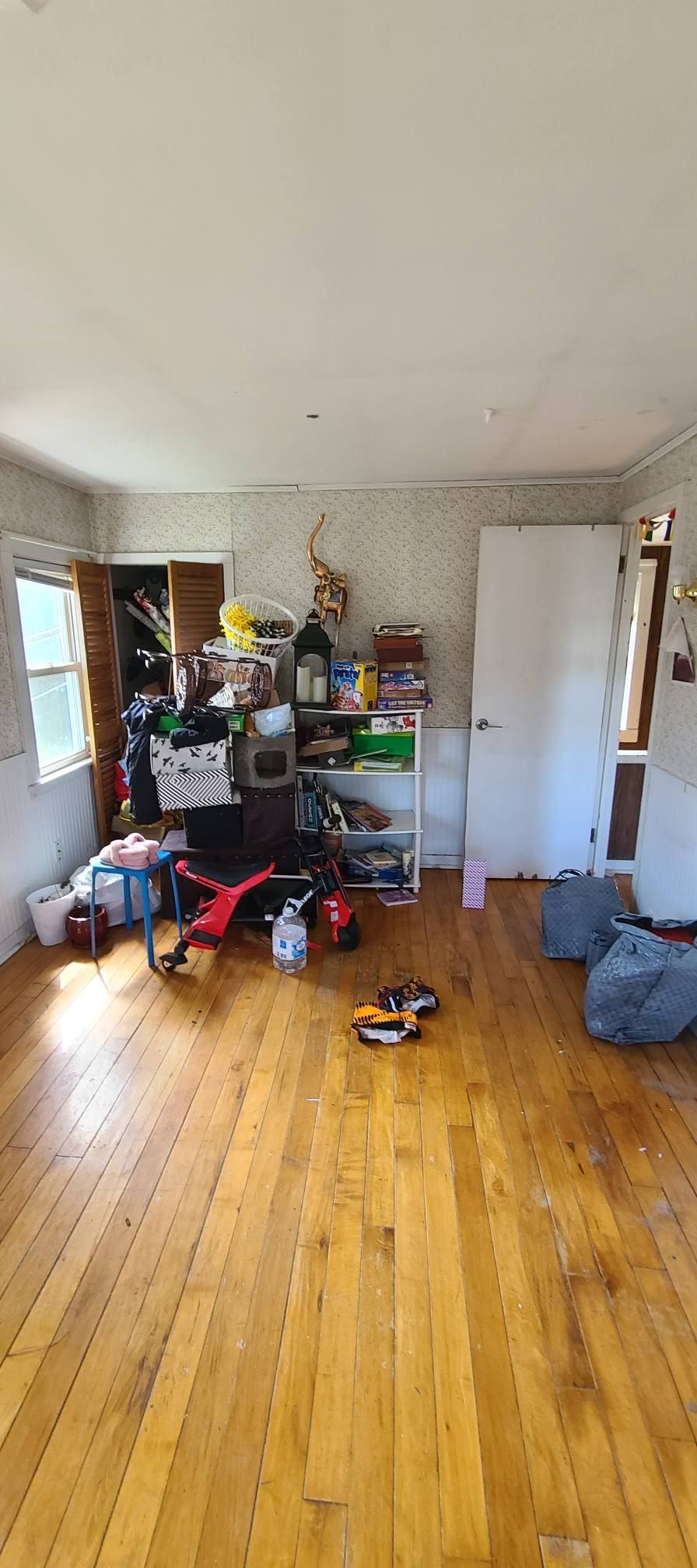 Cluttered room with hardwood floors, shelves of items, scattered shoes, and a leaning whiteboard near the wall