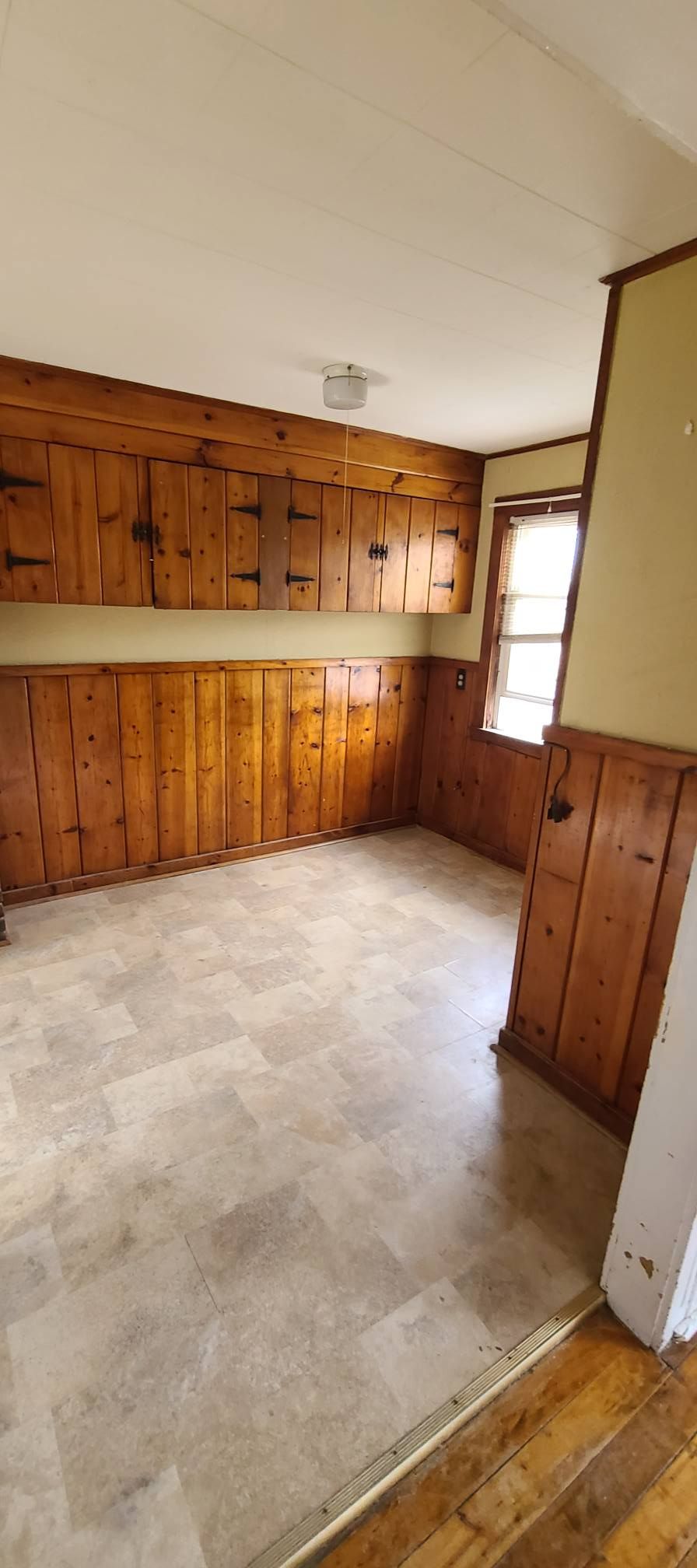 Empty room with wood-paneled walls, beige carpet, and a window on the right.