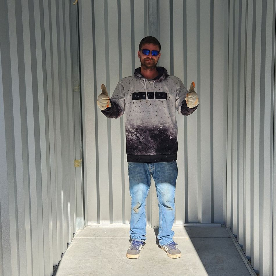 Person standing in a corrugated metal container, wearing sunglasses, thumbs up, in sunlight