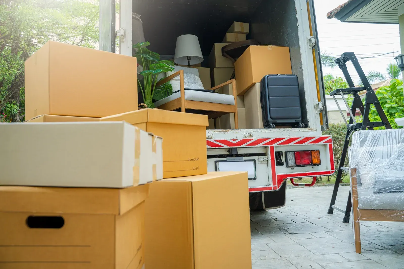Stacked moving boxes and furniture on a truck in a driveway, ready for unloading.