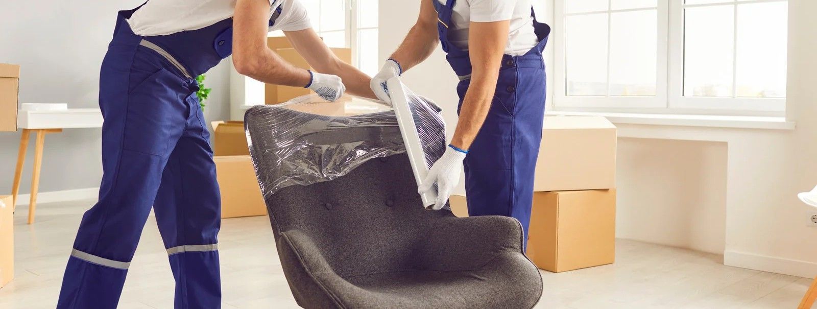 Two people moving a dark couch in a bright room with large windows