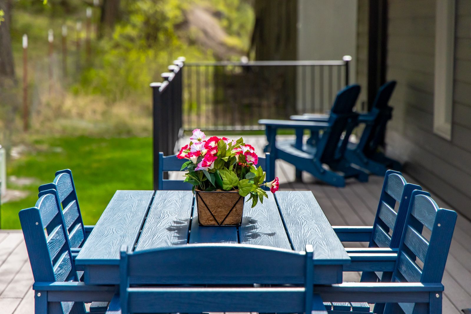 Blue outdoor patio table and chairs with a potted flower centerpiece beside a house