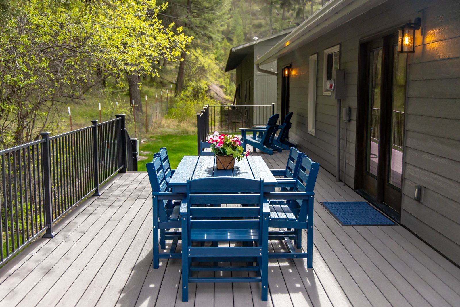 Blue outdoor dining set on a wooden deck beside a house, with a wooded yard in the background