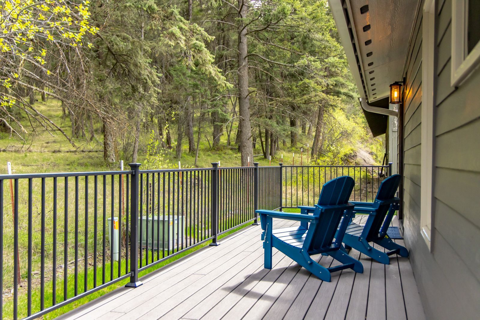 Blue chairs on a porch overlooking a green forest and stream through black railing.