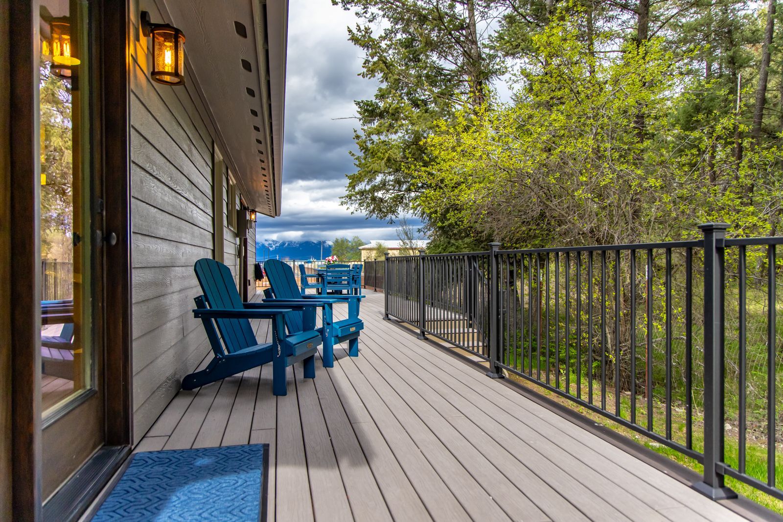 Wooden deck with blue chairs, railing, and trees overlooking a distant lake under a cloudy sky