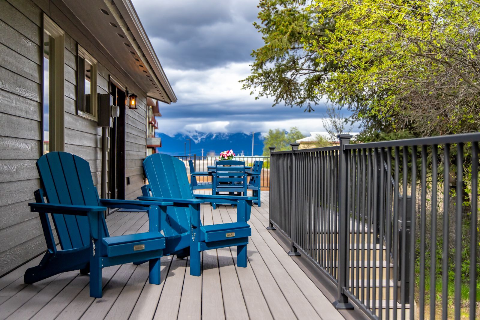 Blue Adirondack chairs on a wooden deck overlooking mountains under cloudy skies