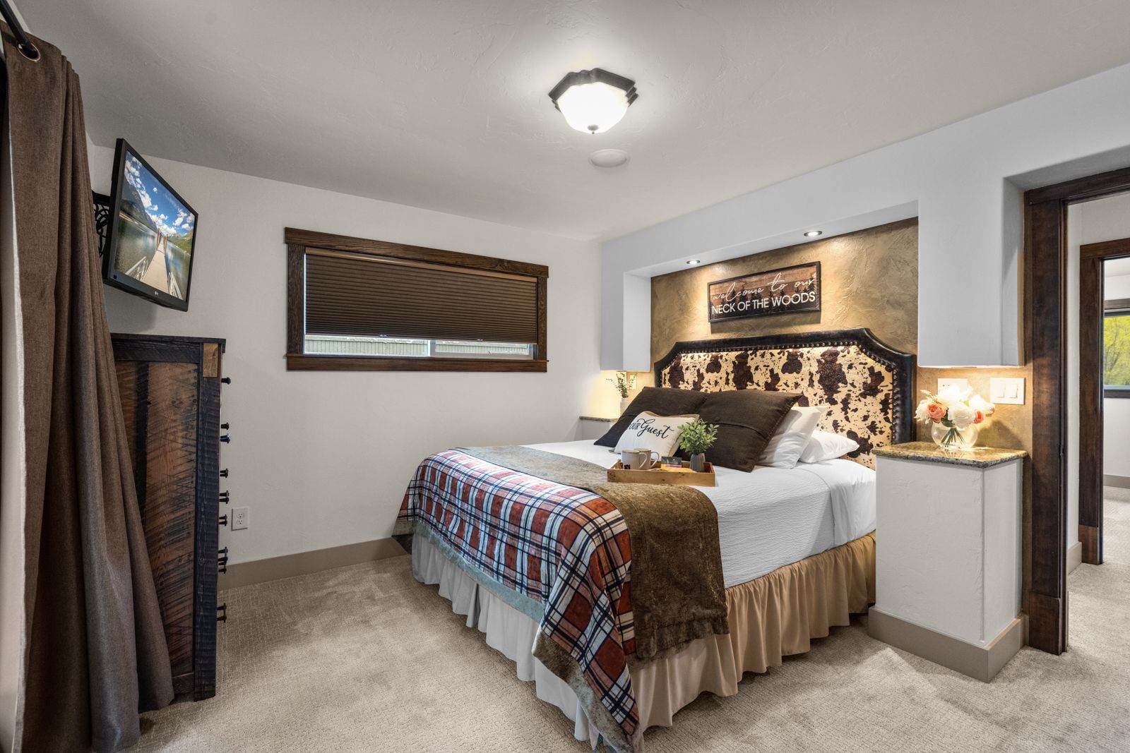 Cozy bedroom with a made bed, neutral carpet, wall art, and warm lamp lighting