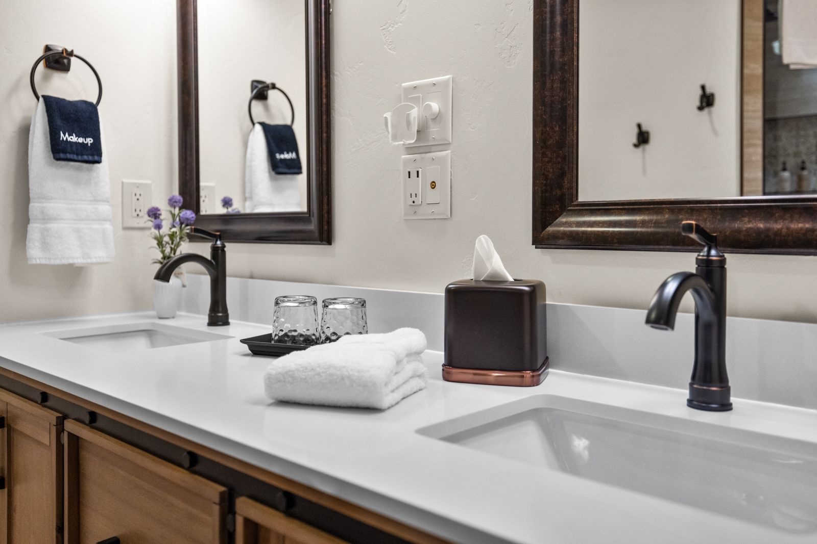Modern bathroom vanity with two sinks, mirrors, dark faucets, and neatly folded towels.