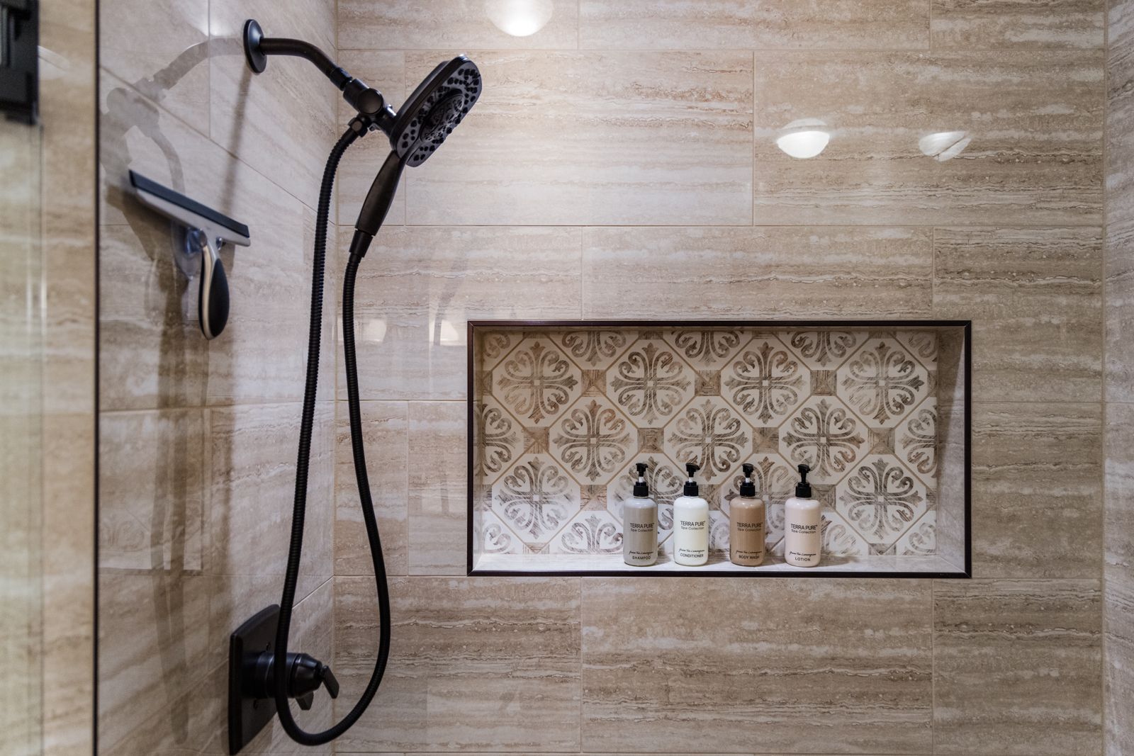 Bathroom shower with handheld showerhead and built-in shelf of toiletries on beige tile wall
