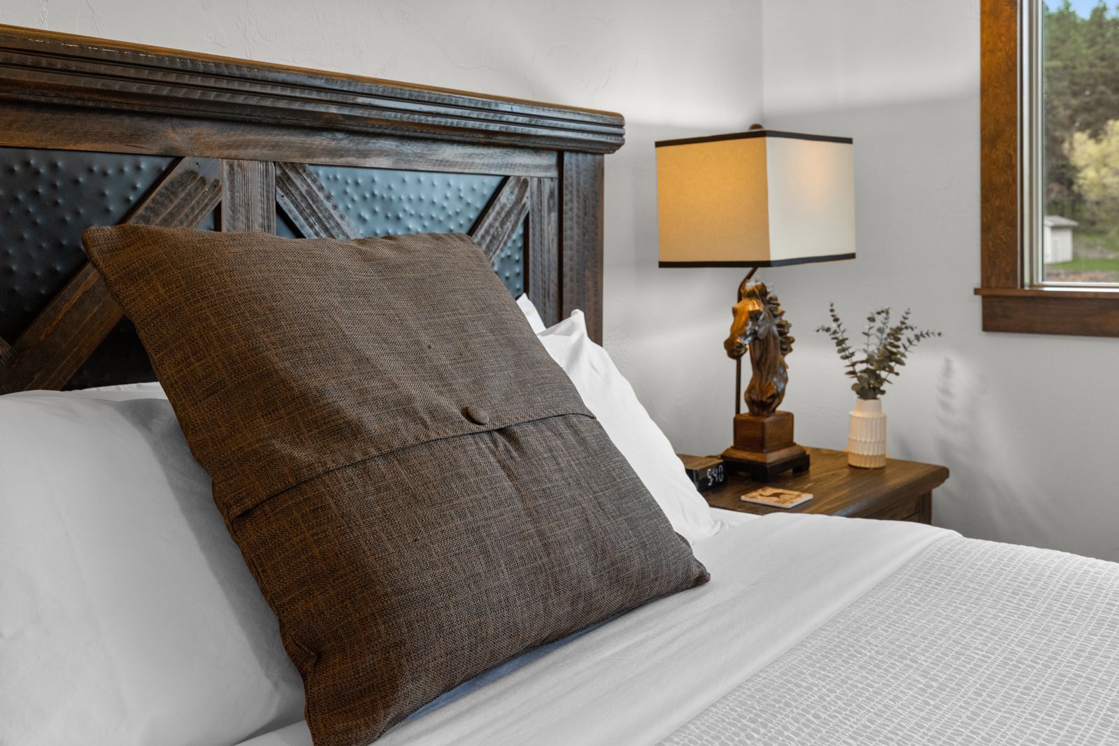 Close-up of a neatly made bed with brown pillow, bedside lamp, and window in a cozy bedroom