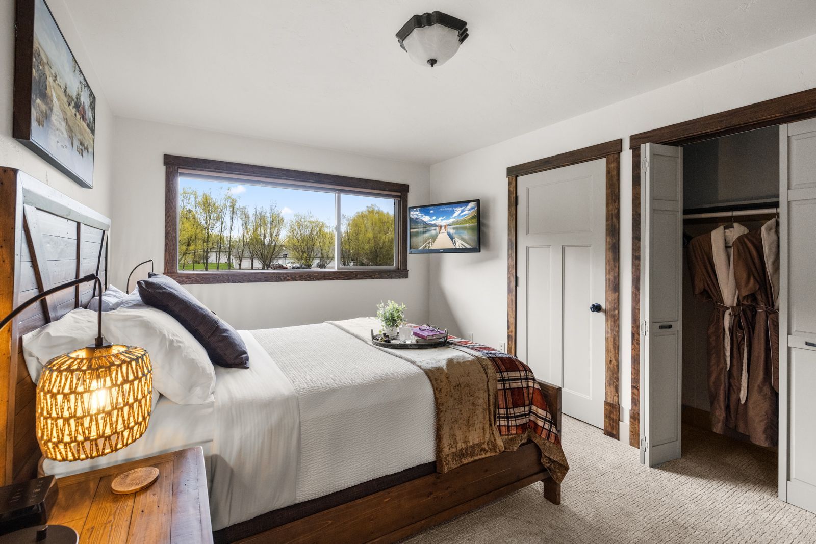 Bright bedroom with a bed, open closet, wall art, and large window overlooking trees