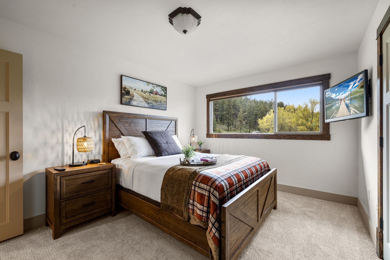 Cozy bedroom with wooden bed, nightstand, large window, and wall-mounted TV