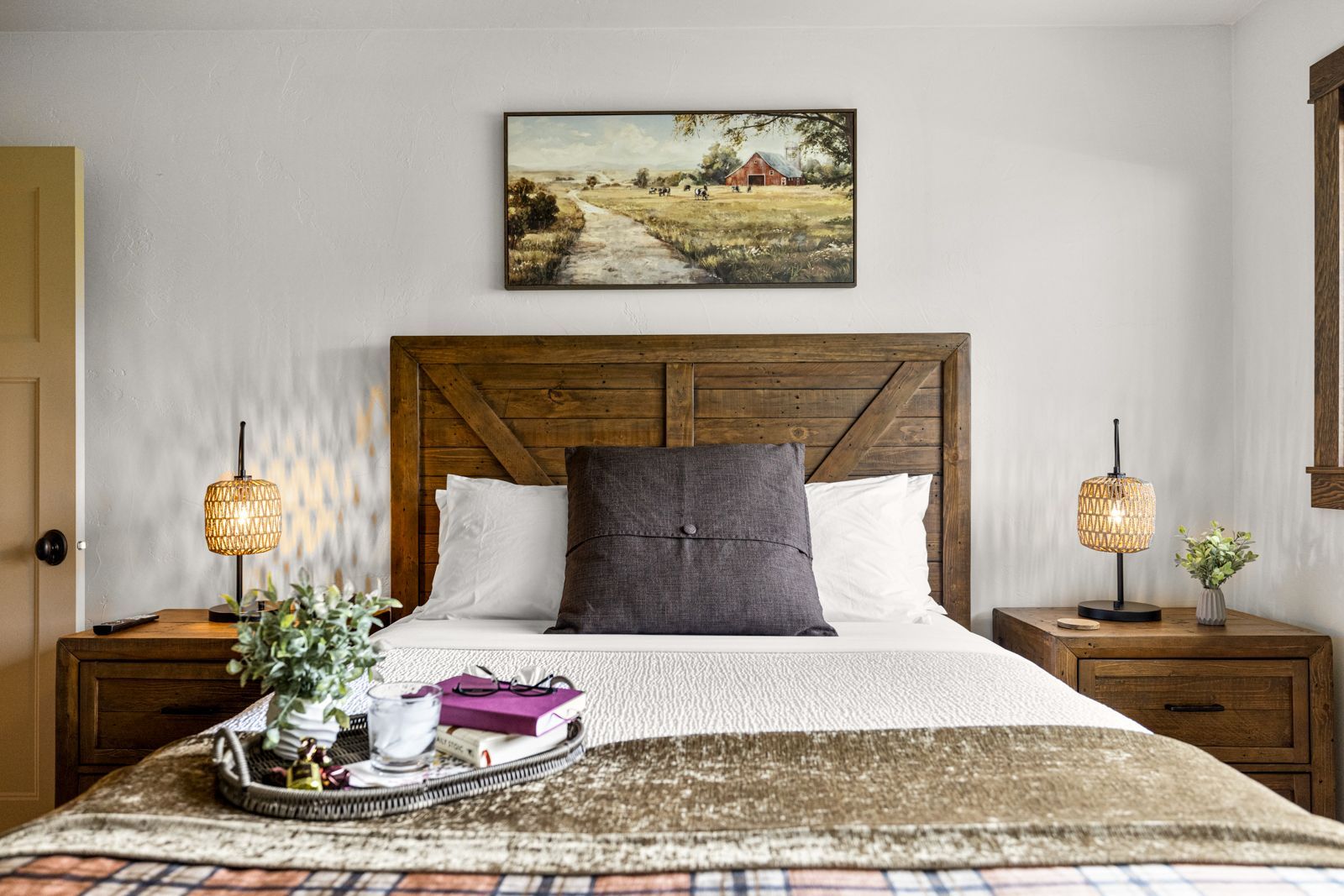 Cozy bedroom with a wooden bed, white bedding, bedside lamps, and a landscape painting above the headboard